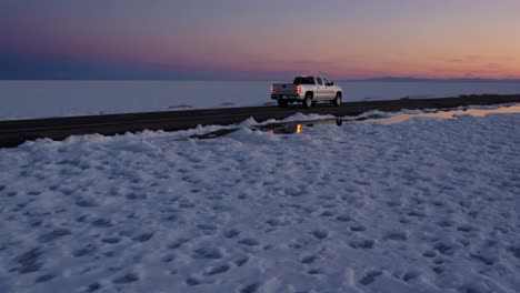 pickup truck driving on a road through a salt flat at sunset