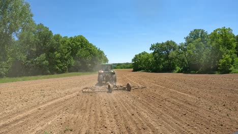 POV---Folgen-Sie-Einem-Traktor,-Der-An-Einem-Sonnigen-Tag-Im-Mittleren-Westen-Eine-Egge-Durch-Ein-Feld-Zieht,-Um-Erdklumpen-Aufzubrechen