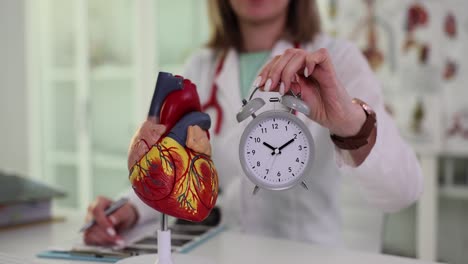 doctor holding heart model and alarm clock