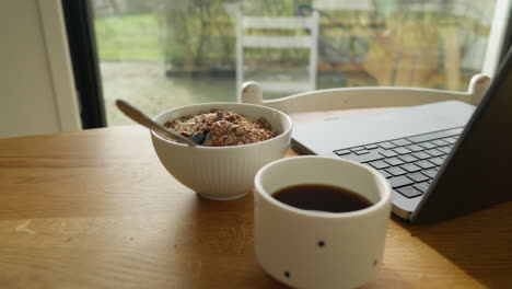 breakfast scene with cereal bowl, coffee, and laptop on a wooden table