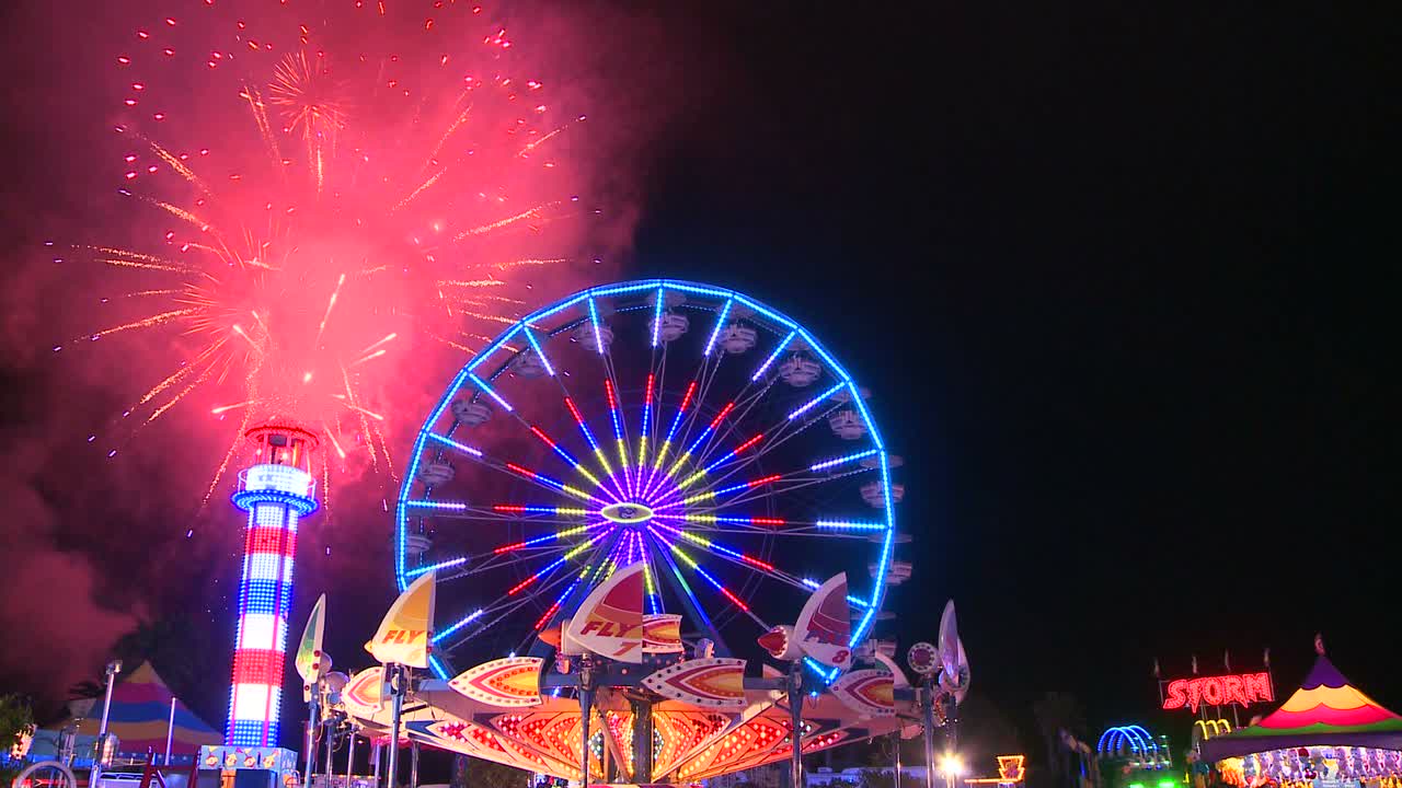 Fireworks explode in the night sky behind a ferris wheel at a carnival or state fair 4