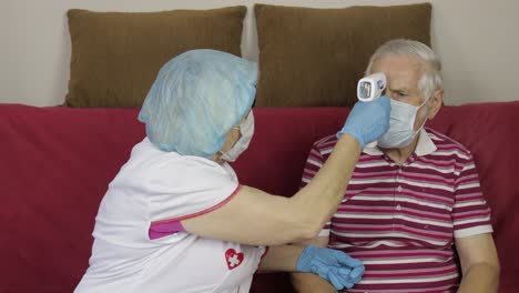 nurse measures temperature with non-contact electronic thermometer of sick grandfather. coronavirus