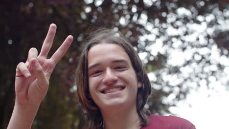 Close-up-of-smiling-male-teenager-looking-at-camera-and-showing-peace-sign