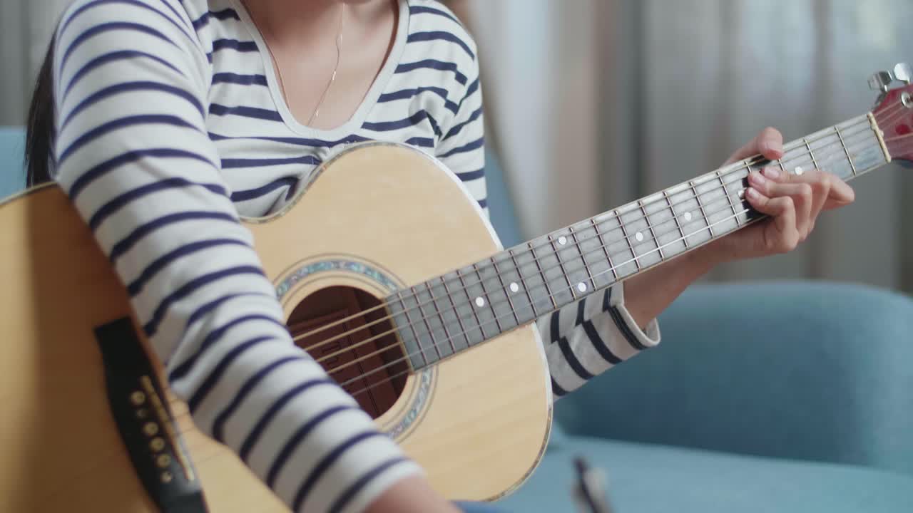 primer plano de una compositora asiática con una guitarra celebrando por terminar de componer música en papel en casa