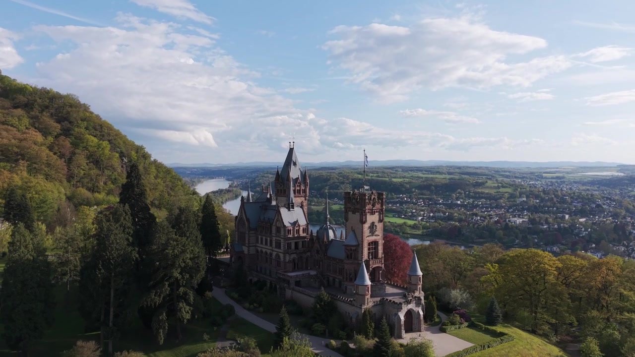 Vista drone dello storico Castello di Schloss Drachenburg circondato da una foresta verde che si affaccia sulla valle del fiume Reno in Germania. Ripresa aerea all'indietro