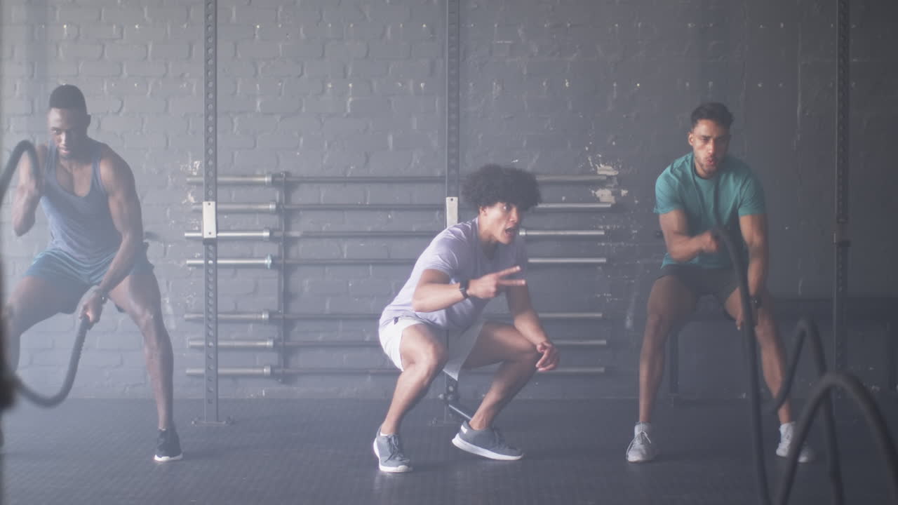 Group of diverse men training with battle ropes in gym