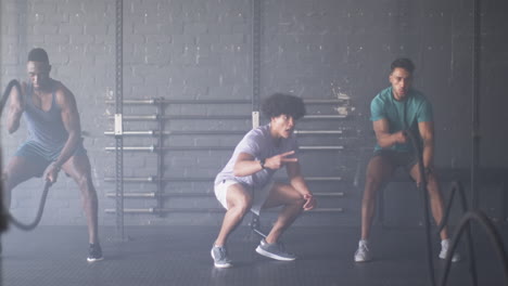 group of diverse men training with battle ropes in gym