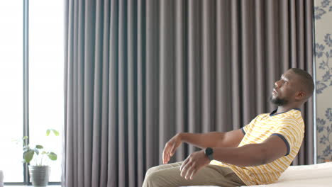relaxing at home, african american man stretching on bed in comfortable setting