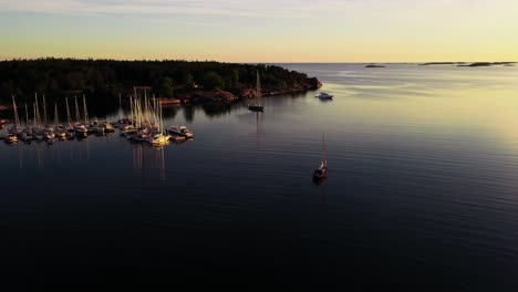 Aerial-view-over-a-sailboat-passing-the-Jussaro-guest-harbor,-sunny-evening-in-Finland