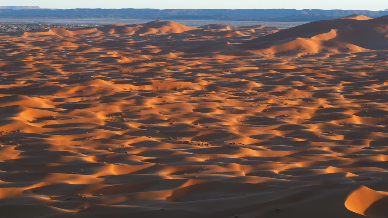 una foto panorámica de las dunas de merzouga, marruecos con una caravana de camellos pasando