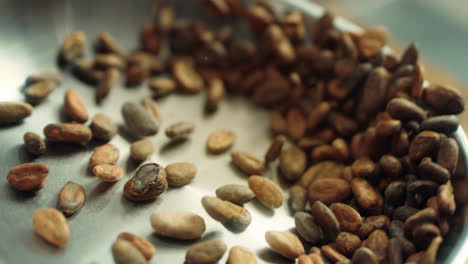 close up cocoa beans tossing in metal pan in slow motion.