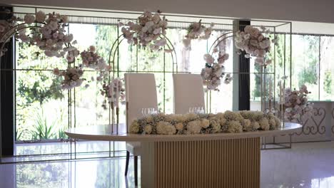 elegant indoor wedding setup with floral arch and table, bright natural light streaming in