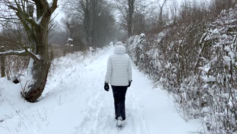 woman in white winter coat walking through snowdrift tracks in winter forest