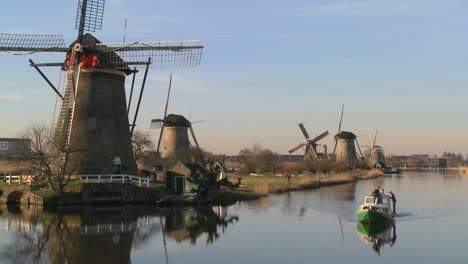 a boat moves along a canal in holland with windmills nearby 3