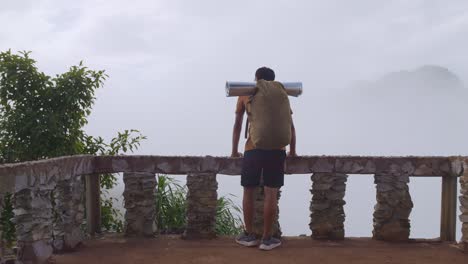 asian hiker male standing on a veranda cliff enjoys seeing beautiful view of top foggy mountain. a man from the tent view of the mountain