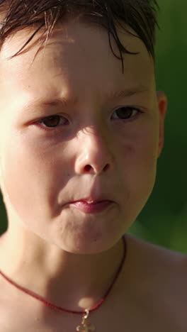 portrait of a cute hungry boy outdoors. little boy with wet hair is eating something on blurred background in summer. vertical video