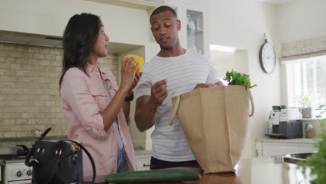 feliz pareja biracial desempaquetando comestibles en la cocina