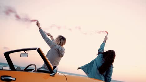 young women with vintage convertible car celebrating with smoke bombs