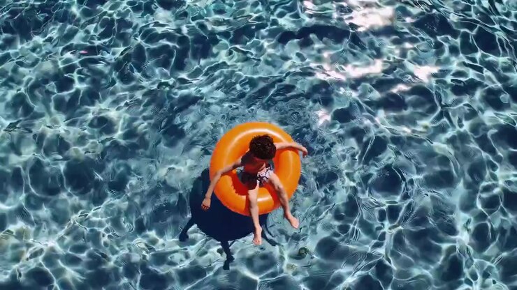 Young Boy Floating on an Orange Inflatable Ring in a Sunny Swimming Pool