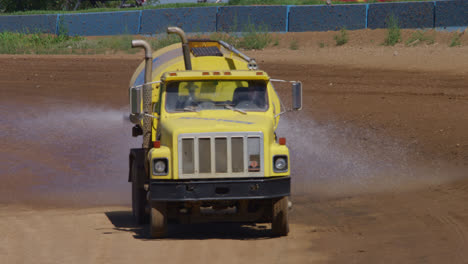 yellow water truck spraying down a dirt race track in slow motion