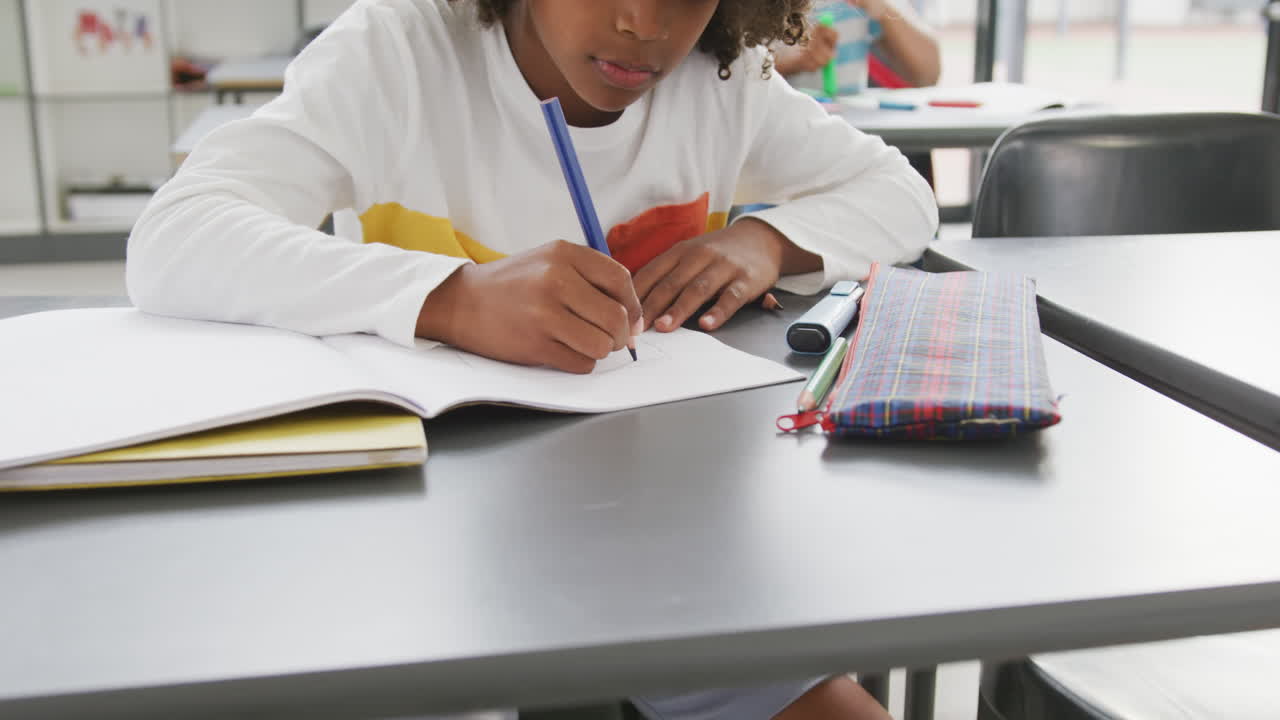 video de un escolar afroamericano sentado en un escritorio escribiendo en clase en la escuela
