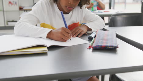 video de un escolar afroamericano sentado en un escritorio escribiendo en clase en la escuela