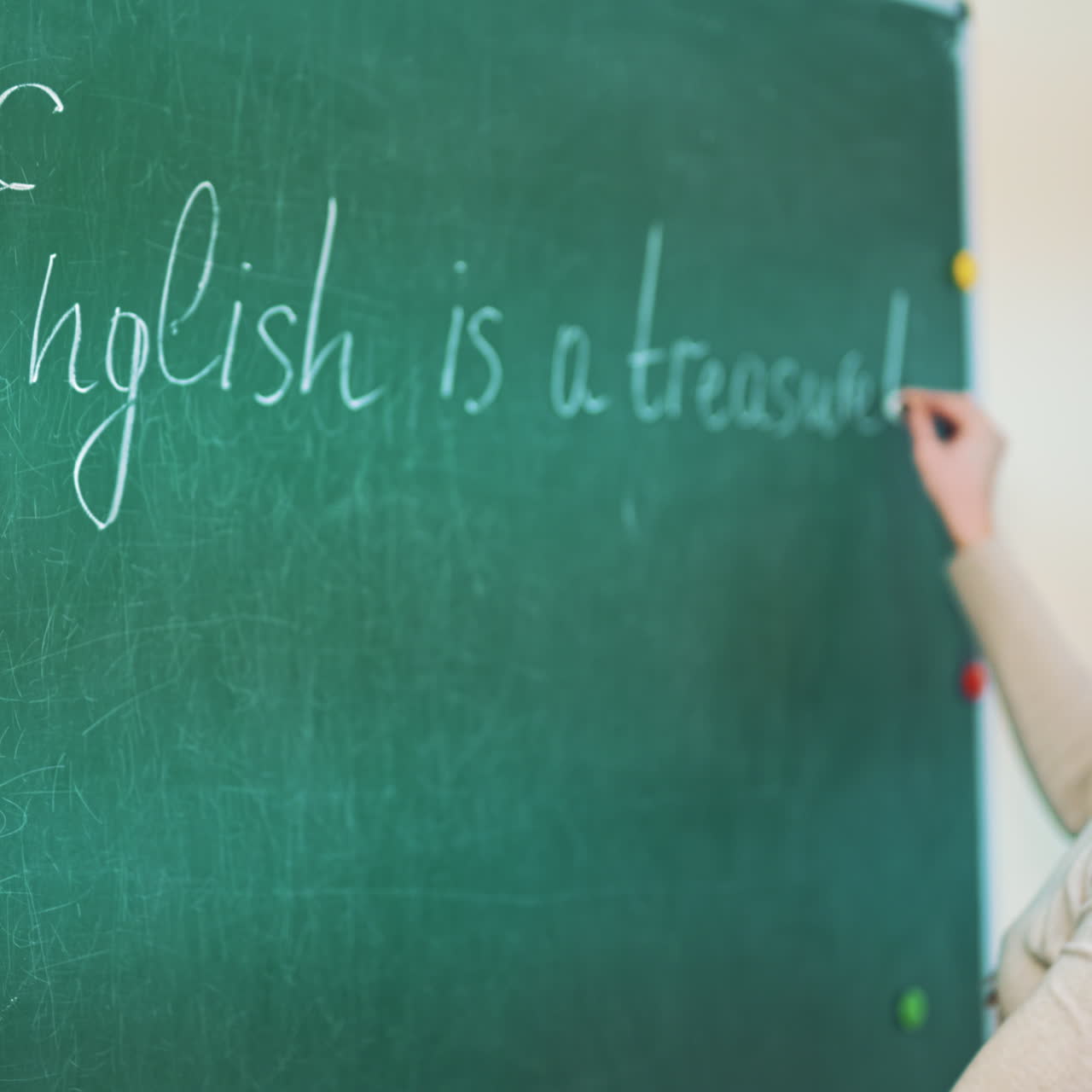 Young pedagogue writes on a blackboard with a chalk in the educational center. Attractive teacher is writing English words on a board in the classroom.
