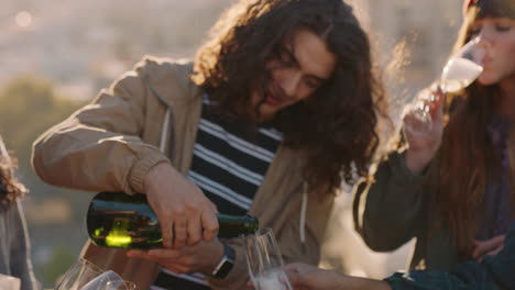 Joven-Sirviendo-Champán-Grupo-De-Amigos-Celebrando-En-La-Azotea-Bebiendo-Alcohol-Divirtiéndose-Juntos-Disfrutando-Celebrando-Las-Vacaciones-Al-Atardecer