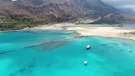 balos beach in crete greece with  turquoise waters and a tourist transport ship and it's dinghy boat attached, aerial flyover reveal shot
