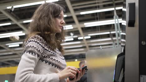 brunette woman pays at atm using pay pass in smartphone