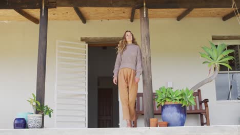 smiling caucasian woman standing, leaning outside house looking out from terrace