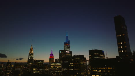 Descending-footage-of-high-rise-buildings-with-lighted-windows.-Iconic-downtown-skyscrapers-against-colourful-sky-at-dusk.-Manhattan,-New-York-City,-USA