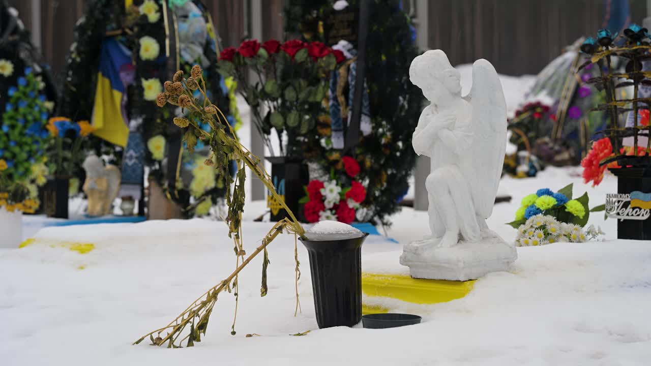 On a dull winter day, a wilted bouquet of flowers is placed in front of an angel statue to honor a fallen Ukrainian soldier at Irpin Cemetery, Ukraine, who perished in the Ukraine-Russia war.