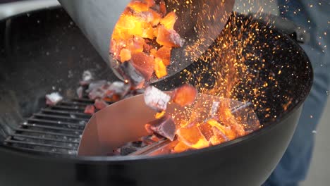 Flaming-coals-are-added-to-charcoal-grill,-slow-motion