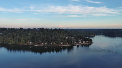 drone footage of puget sound with the peak of mount rainier in the background, framed by tall pines and rural lake homes