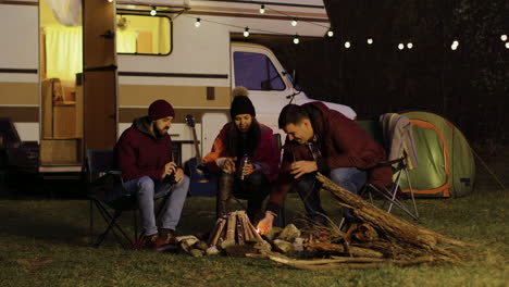 man helping friend to light the camp fire in front of retro camper