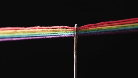 video of micro of rainbow coloured threads going through needle with copy space on black background