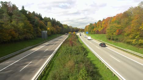 View-over-a-freeway-with-driving-cars-framed-by-autumn-colored-trees,-dynamic-zoom