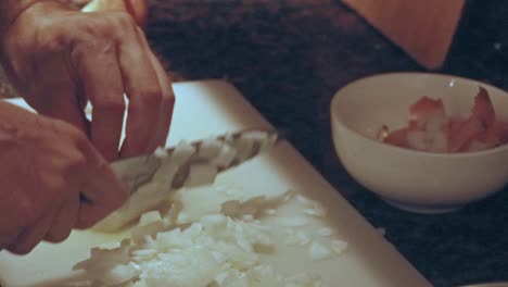 close up to hands swiftly chopping and mincing white onion in a dimly lit kitchen counter