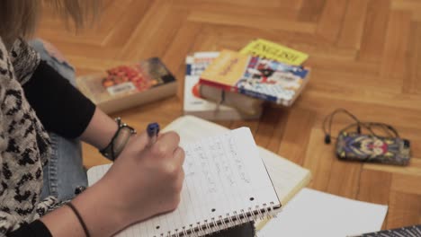 escribiendo notas en el cuaderno, detalle de la mano sosteniendo un bolígrafo, libros en un fondo, toma estática