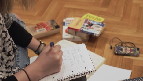 writing a notes to notebook, detail of hand holding a pen, books in a background, static shot