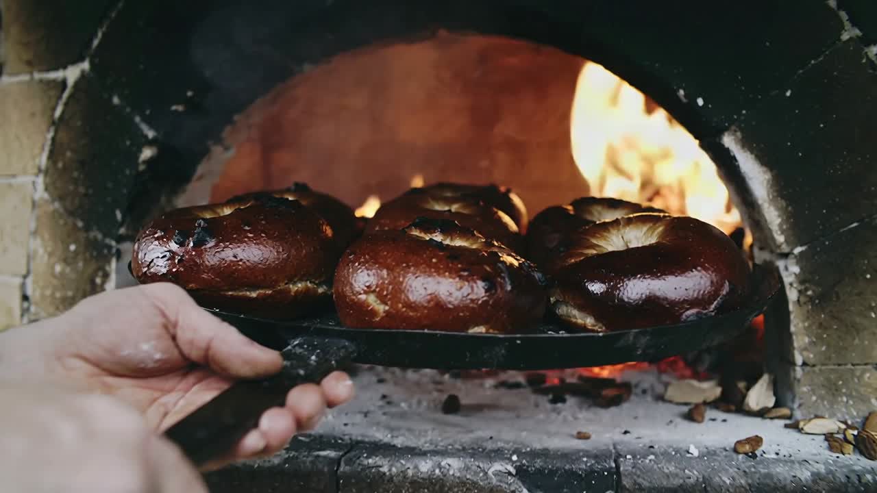 帽子とエプロン姿のパン職人が、焼き色がつき始めた5つのパンを、ピールを滑らせるようにして薪窯から取り出している。