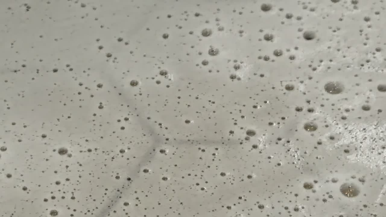 Closeup texture of soap bubbles on wet concrete floor with water droplets and industrial lighting