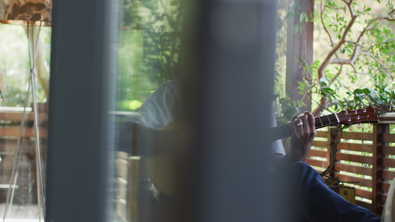 아쿠스틱 기타 를 연주 하는 발코니 에 앉아 있는 사려 깊은 아프리카계 미국인 노인