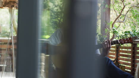 thoughtful african american senior man sitting on balcony playing acoustic guitar