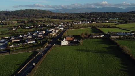 descending aerial view overlooking rural welsh village surrounded by agricultural farmland countryside