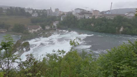 rhine falls on rainy day and town panorama, rapid river, waterfall