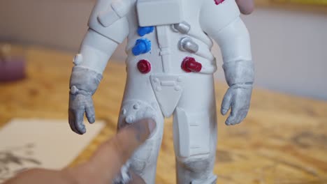 artist painting astronaut figure with fingers grey paint