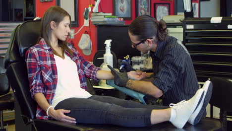 una mujer se sienta en una silla con un tatuaje en un salón filmado en r3d