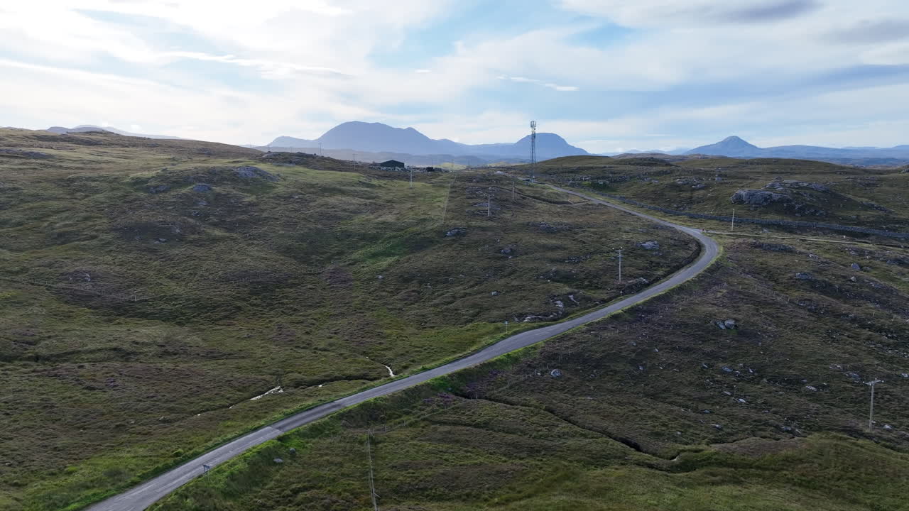 Drone aerial view of a winding road through rugged hills near Oldshoremore on the North Coast 500. Scenic Scottish Highlands landscape with mountains in the distance under soft afternoon light